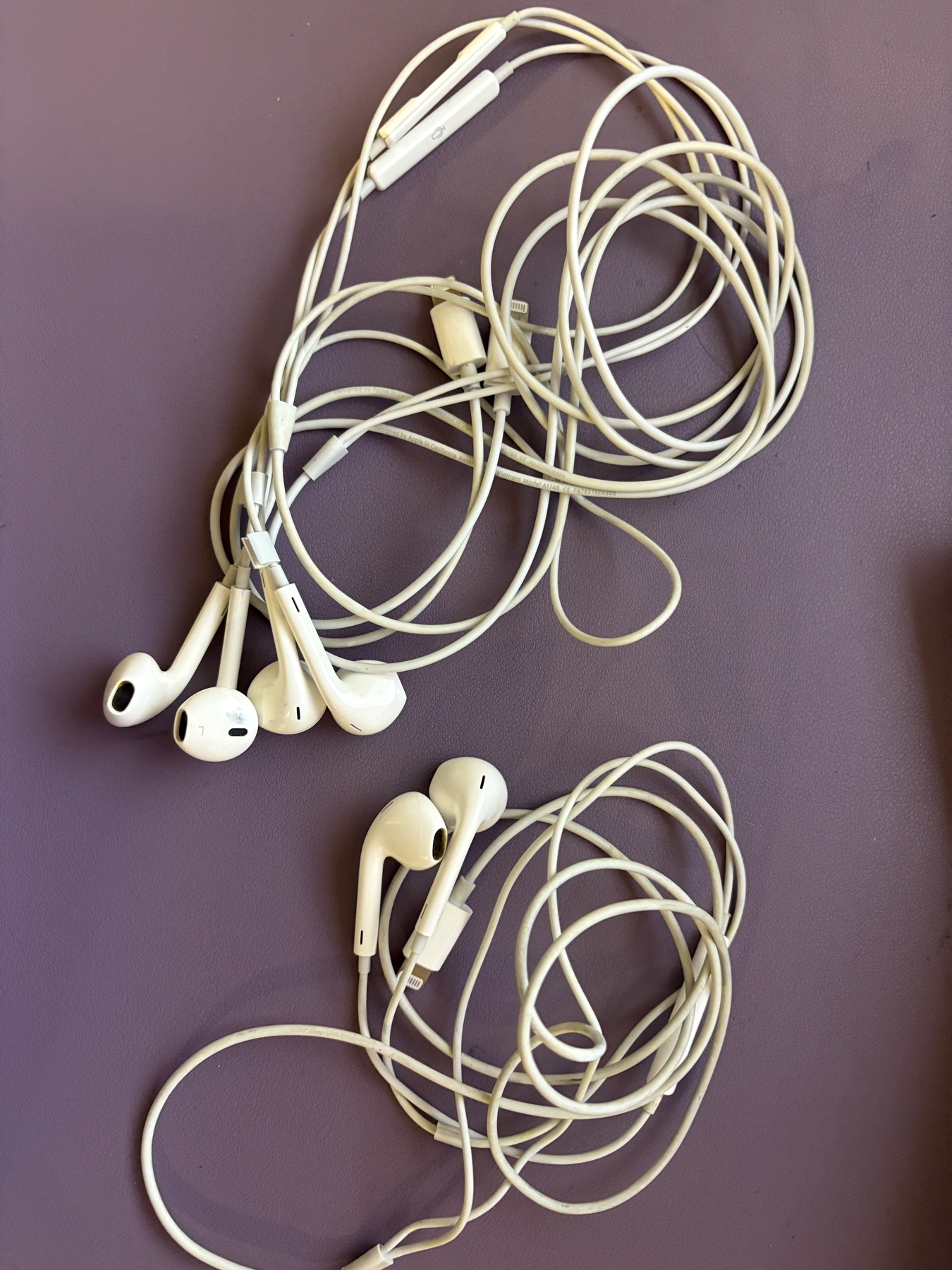 Three pairs of white wired earphones with tangled cords on a purple surface.